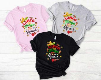 May include: Three t-shirts with a Cinco de Mayo theme. The shirts are pink, gray, and black. Each shirt has a graphic of a sombrero, maracas, and a guitar with the text "Cinco de Mayo Squad".