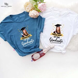 May include: Two blue and white t-shirts with a photo of a graduate wearing a cap and gown. The text on the shirts reads "Proud Dad of the Graduate" and "Proud Mom of the Graduate".