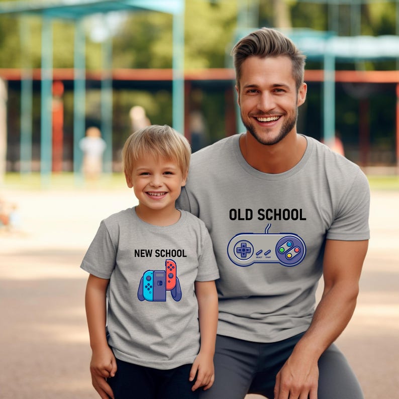 Op de afbeelding: Twee grijze t-shirts met bijpassende ontwerpen. E&eacute;n shirt zegt "OLD SCHOOL" met een controller-afbeelding. De andere zegt "NEW SCHOOL" met een gameconsole-afbeelding. De shirts worden gedragen door een man en een kind.