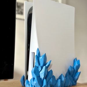May include: A white console stand with a blue crystal-like design. The stand is made of plastic and has a modern look.