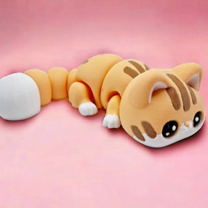 May include: A small, orange and white cat figurine with a segmented body. The cat is lying on its side with its head resting on the ground. The cat has black eyes and a white nose.