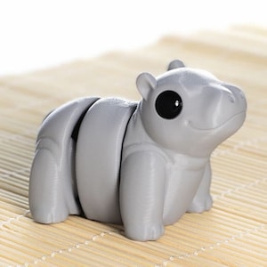 May include: A gray, segmented, articulated toy hippopotamus with black eyes. The toy is sitting on a light brown bamboo mat. The text "Baby Hippo" is printed below the toy.