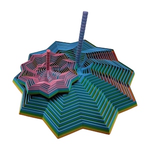 May include: A colorful, abstract sculpture featuring layered, star-shaped forms in shades of blue, green, pink, and orange. Two pink and blue cylindrical elements rise from the structure. The artwork has a geometric, modern aesthetic.