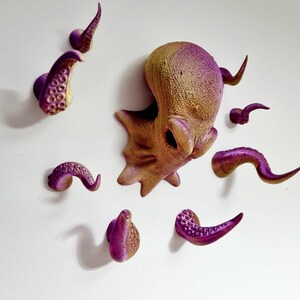May include: A set of eight purple and gold octopus wall hooks. The hooks are shaped like tentacles and are arranged in a circle around a larger octopus head.