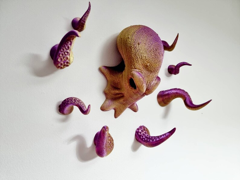 May include: A set of eight purple and gold octopus wall hooks. The hooks are shaped like tentacles and are arranged in a circle around a larger octopus head.