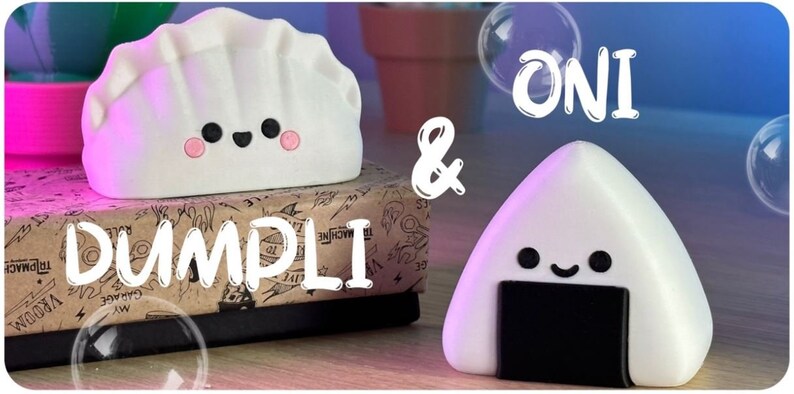 May include: White and black cartoon characters shaped like a dumpling and a rice ball. The dumpling has a pink blush and the rice ball has a black seaweed wrapper. The text "ONI & DUMPLI" is written in white on a brown background.
