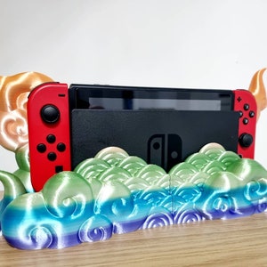 May include: A 3D printed Nintendo Switch stand with a colorful cloud design. The stand features two horns on either side and a slot for the Switch console.