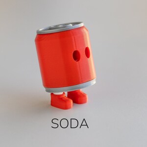 Puede incluir: Una figura caprichosa de lata de refresco naranja con dos agujeros en forma de ojos y pies a juego. La lata tiene una parte superior e inferior plateadas. La palabra "SODA" está impresa en negro debajo.