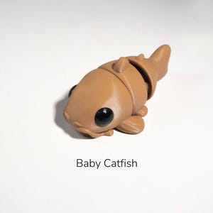 May include: A brown, cartoon-style catfish figurine with large black eyes. The figurine is made of plastic and has a segmented body.
