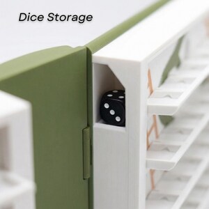 May include: A close-up of a dice storage box. The box is white and olive green with the words "Dice Storage" printed on the top left. A black die with white dots is visible inside the box.