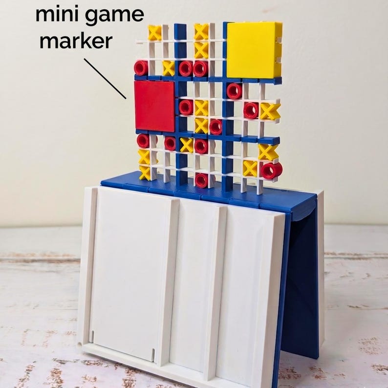 May include: A tic-tac-toe game board featuring a white grid structure with blue supports, yellow X markers, and red O markers. A large red square and a large yellow square are attached to the grid. The text mini game marker points to the grid.