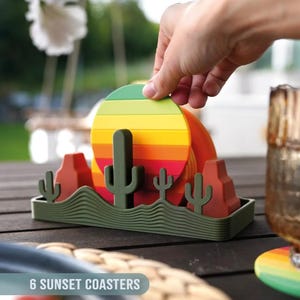 May include: A set of six sunset-themed coasters. Each coaster features a colorful, striped design resembling a sunset. The set includes a green holder with cactus and desert landscape details. The text "6 SUNSET COASTERS" is visible.