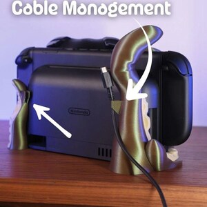 May include: A cable management system for a Nintendo Switch. The system is designed to look like an octopus, with a gold-colored tentacle holding the charging cable. The words "Cable Management" are at the top of the image.