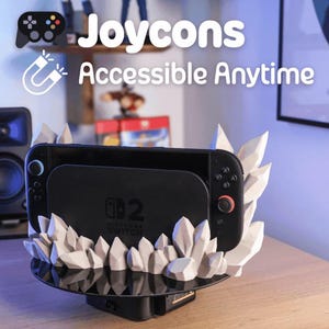May include: A black Nintendo Switch console is docked in a custom stand. The stand features a black base and is decorated with white, crystal-like structures. The text "Joycons Accessible Anytime" is displayed above the console.
