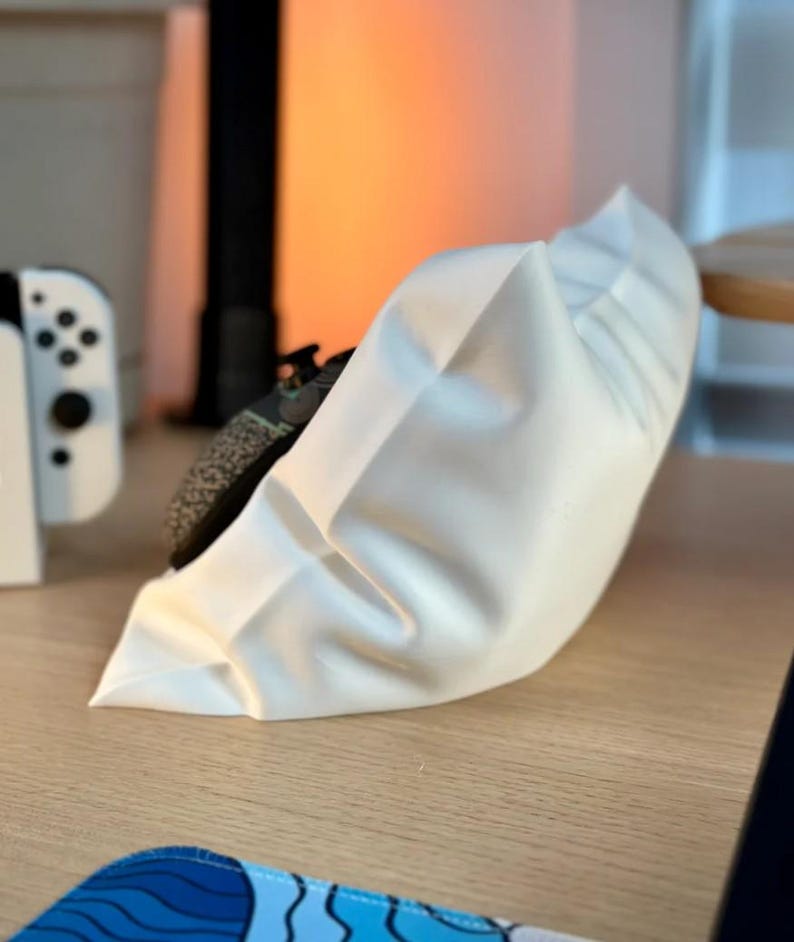 May include: A white, fabric pillow with a ruffled edge. The pillow is sitting on a wooden surface.