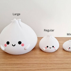 May include: Three white ceramic figurines shaped like steamed buns with cute faces. The figurines are labeled "Large", "Regular", and "Mini" from left to right.