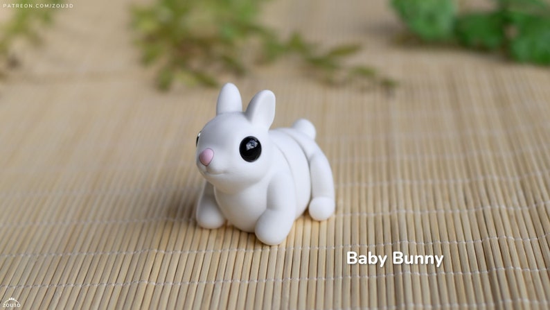 May include: A small, white ceramic bunny figurine with black eyes and a pink nose. The bunny is sitting on a woven bamboo mat.
