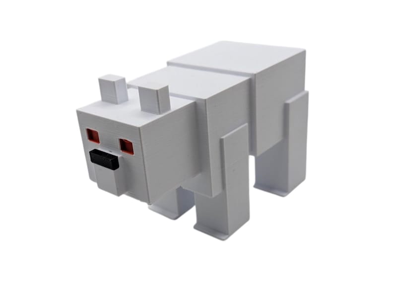 May include: A white, blocky polar bear figurine with red eyes and a black nose. The toy is made of geometric shapes, resembling a pixelated design. The bear has four rectangular legs and two small rectangular ears.