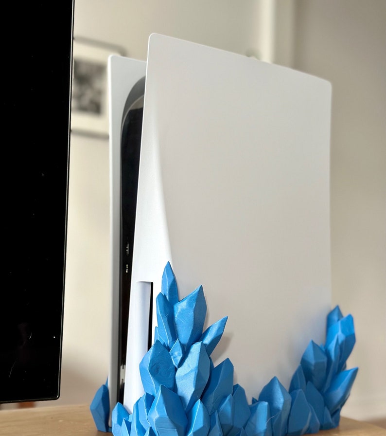 May include: A white console stand with a blue crystal-like design. The stand is made of plastic and has a modern look.