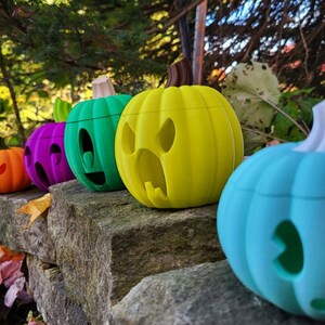May include: Five colorful jack-o'-lantern pumpkins with different facial expressions. The pumpkins are arranged in a row on a stone wall. The pumpkins are painted in shades of orange, purple, green, yellow, and blue.