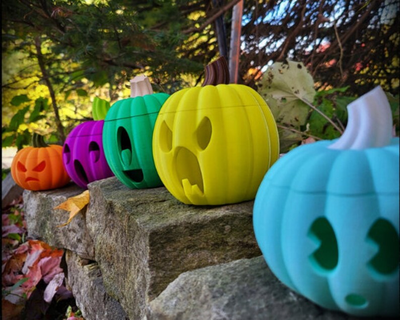 May include: Five colorful jack-o'-lantern pumpkins with different facial expressions. The pumpkins are arranged in a row on a stone wall. The pumpkins are painted in shades of orange, purple, green, yellow, and blue.