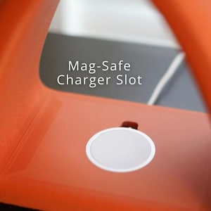 May include: Close-up of an orange Mag-Safe charger slot. The charger has a white circular charging pad. The text "Mag-Safe Charger Slot" is printed in white on the background.