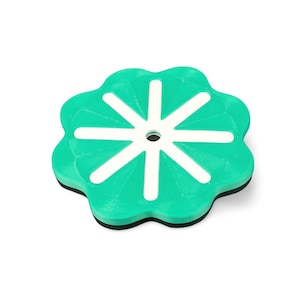 May include: A teal and white coaster with a flower-like design. The coaster has a circular shape with a series of curved edges. White lines radiate from a central hole, creating a starburst pattern. The coaster has a black base.