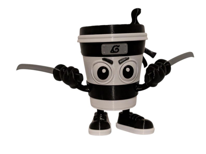 May include: A black and white coffee cup figurine with cartoon eyes, a ninja headband, and two gray swords. The cup has black sneakers and arms. The design is a playful take on a ninja theme.
