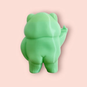 May include: A green 3D printed figurine of a cartoon character. The character is standing with its arms raised and has a round body and a large head.
