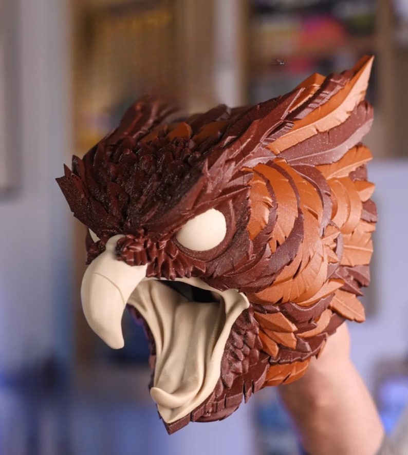 May include: A detailed, brown and tan owl mask with a fierce expression. The mask features textured feathers, large white eyes, and a prominent beak. The mouth is open, revealing a tan interior, creating a striking, realistic appearance. This mask is ideal for cosplay or costume events.