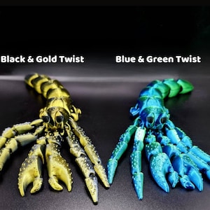 Puede incluir: Dos figuritas de escorpi&oacute;n impresas en 3D, una en negro y oro, la otra en azul y verde. Los escorpiones est&aacute;n en pose con sus garras extendidas.