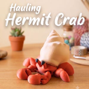 May include: A sculpted red hermit crab figurine with a large, smooth, light beige spiral shell on its back. The crab has two small black eyes on stalks and multiple articulated legs. The text "Hauling Hermit Crab" is displayed above the figure.