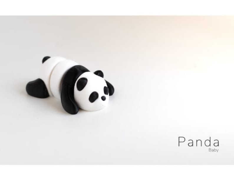 May include: A black and white panda figurine made of clay, lying on its belly with its head turned to the side. The panda has black ears, eyes, and paws. The figurine is on a white background. Panda Baby.