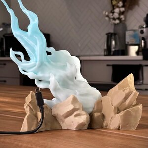 May include: A 3D printed light blue flame sculpture with a cord, sitting on a base of brown rock-like formations.