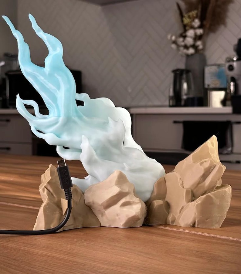 May include: A 3D printed light blue flame sculpture with a cord, sitting on a base of brown rock-like formations.