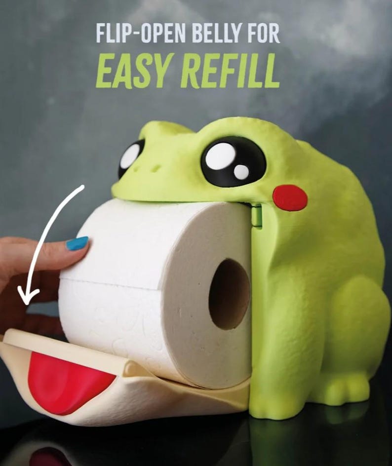 May include: A lime green frog-shaped toilet paper holder with large black and white eyes and a red cheek. The holder has a flip-open belly for easy refill, with the text "FLIP-OPEN BELLY FOR EASY REFILL" in green.