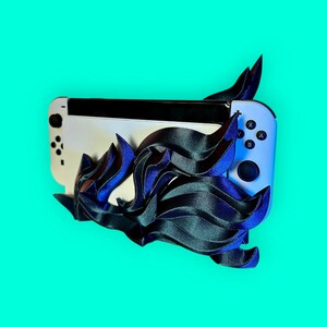 May include: A white Nintendo Switch console with black buttons and a blue and black patterned design. The console is on a bright turquoise background.