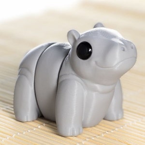 May include: A gray, 3D printed, articulated hippopotamus toy with a black eye. The toy is sitting on a bamboo mat.