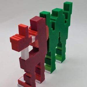 May include: Three pixelated figures in a row. The first is red with white and red accents, the second is green, and the third is also green. The figures have a blocky, geometric design, reminiscent of retro video game characters.