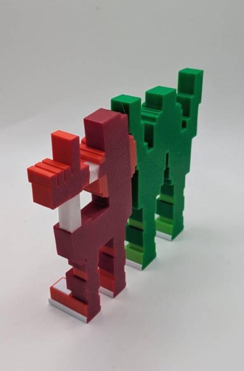 May include: Three pixelated figures in a row. The first is red with white and red accents, the second is green, and the third is also green. The figures have a blocky, geometric design, reminiscent of retro video game characters.