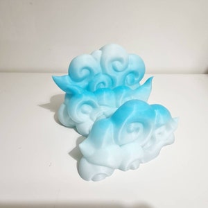May include: Two cloud-shaped decorative objects in shades of blue and white. The clouds have a layered design with swirling details, creating a three-dimensional effect. The objects are likely made of a solid material.