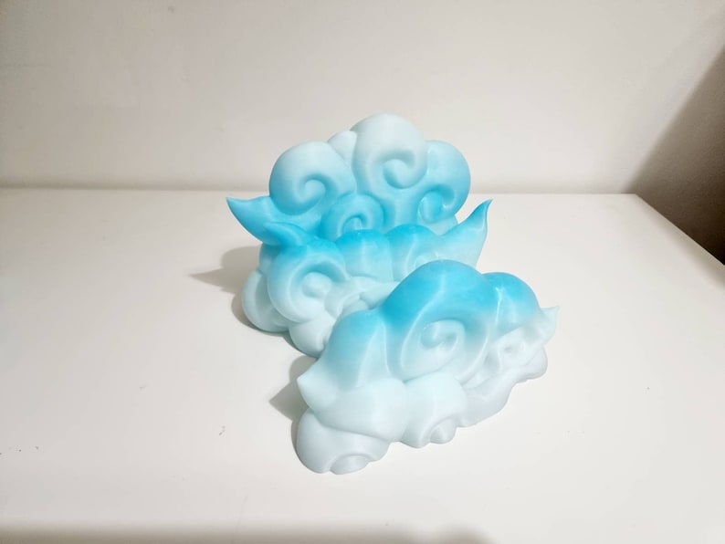 May include: Two cloud-shaped decorative objects in shades of blue and white. The clouds have a layered design with swirling details, creating a three-dimensional effect. The objects are likely made of a solid material.