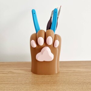May include: A brown 3D printed paw-shaped desk organizer with pink paw prints and two blue tools inside.