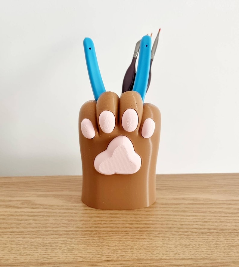 May include: A brown 3D printed paw-shaped desk organizer with pink paw prints and two blue tools inside.