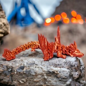 May include: A red origami dragon sculpture on a rock. The dragon is made of folded paper and has a spiky, textured design.
