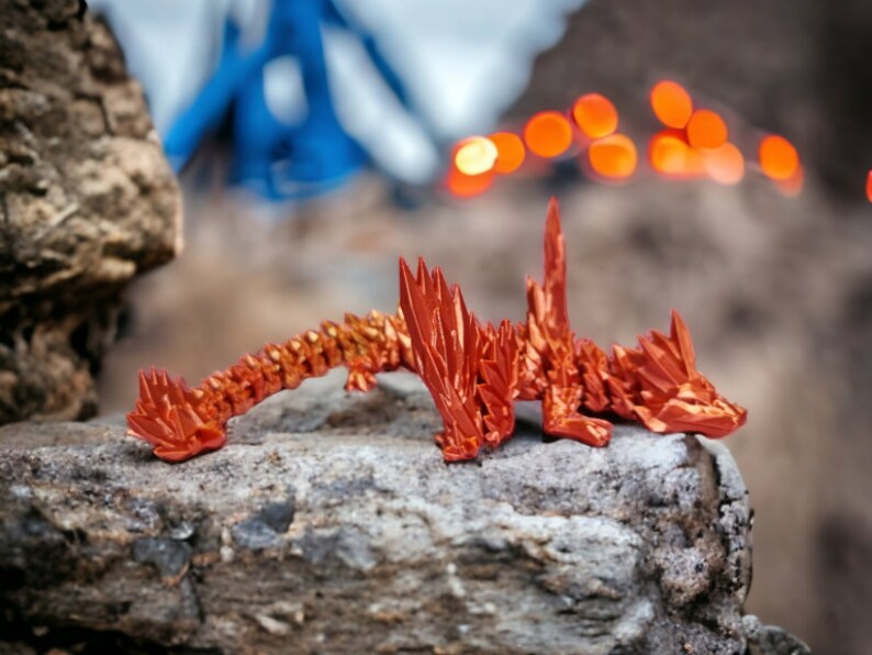 May include: A red origami dragon sculpture on a rock. The dragon is made of folded paper and has a spiky, textured design.