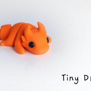 May include: A small, orange, hand-crafted dragon figurine with black eyes. The dragon is curled up in a sleeping position.  Tiny Dragon.
