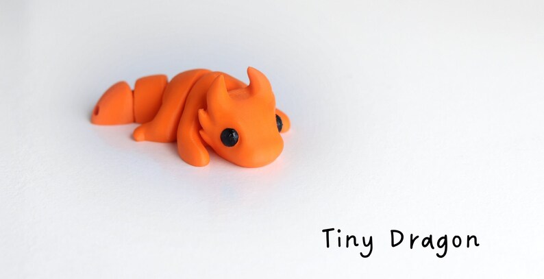 May include: A small, orange, hand-crafted dragon figurine with black eyes. The dragon is curled up in a sleeping position.  Tiny Dragon.