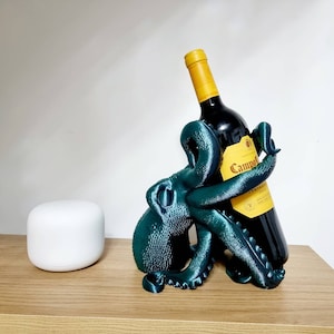 May include: A teal blue octopus shaped wine bottle holder with a bottle of Campo Viejo red wine inside. The bottle holder is on a wooden surface.