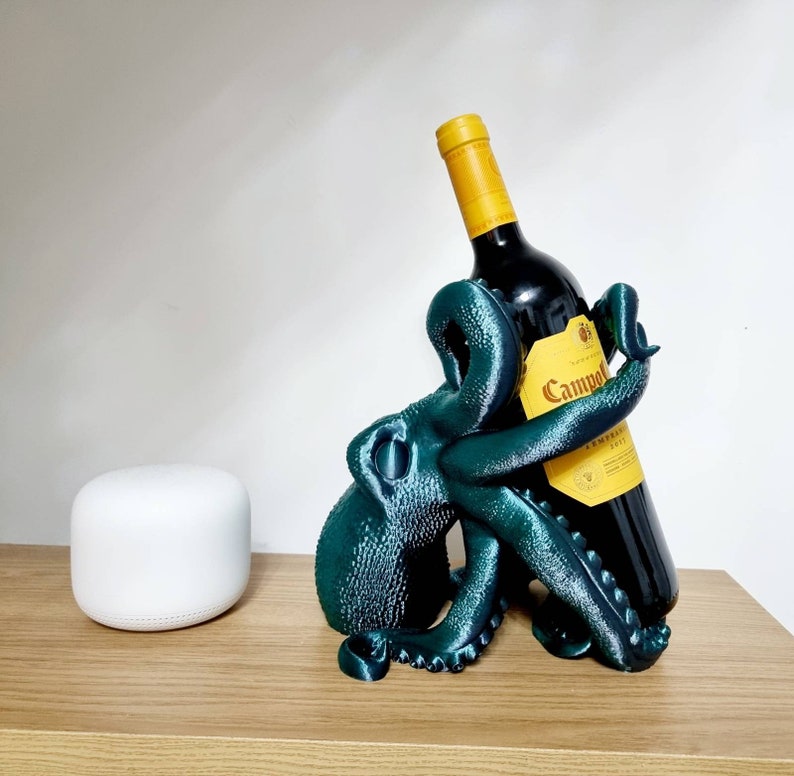 May include: A teal blue octopus shaped wine bottle holder with a bottle of Campo Viejo red wine inside. The bottle holder is on a wooden surface.